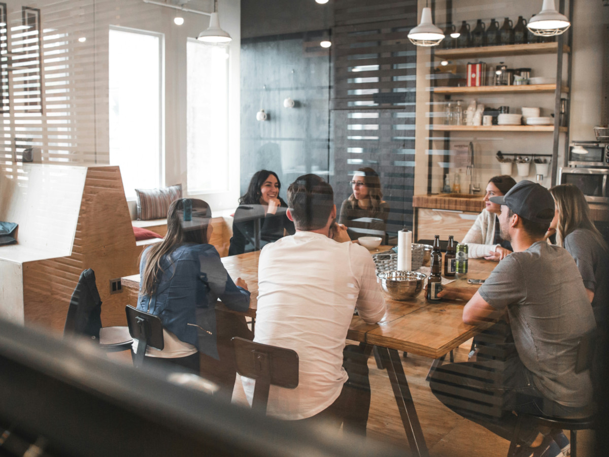 Looking through a window at a group of people sitting around a desk. Photo by Redd Francisco on Unsplash